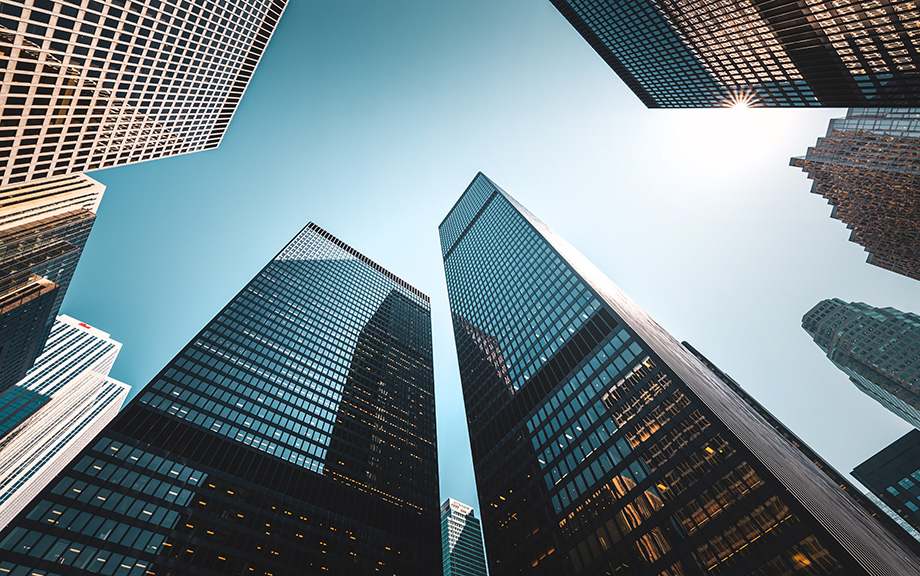 Photo: upward looking at tall glass skyscrapers that are corporate offices against a blue sky.
